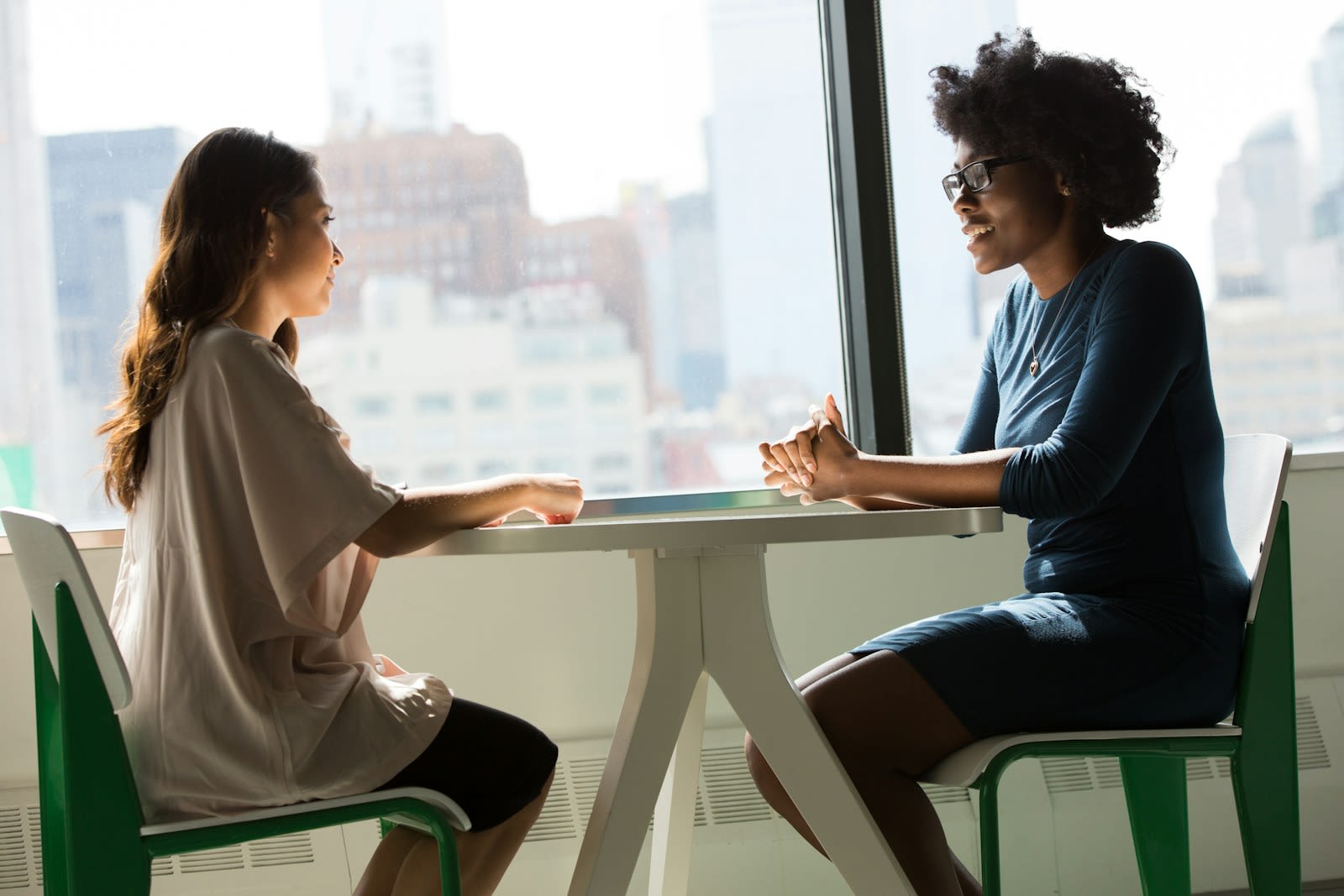Two women talking across a table by a bright window